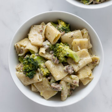 rigatoni pasta with sausage and broccoli with a cream sauce in a white bowl.