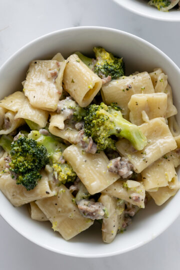 rigatoni pasta with sausage and broccoli with a cream sauce in a white bowl.