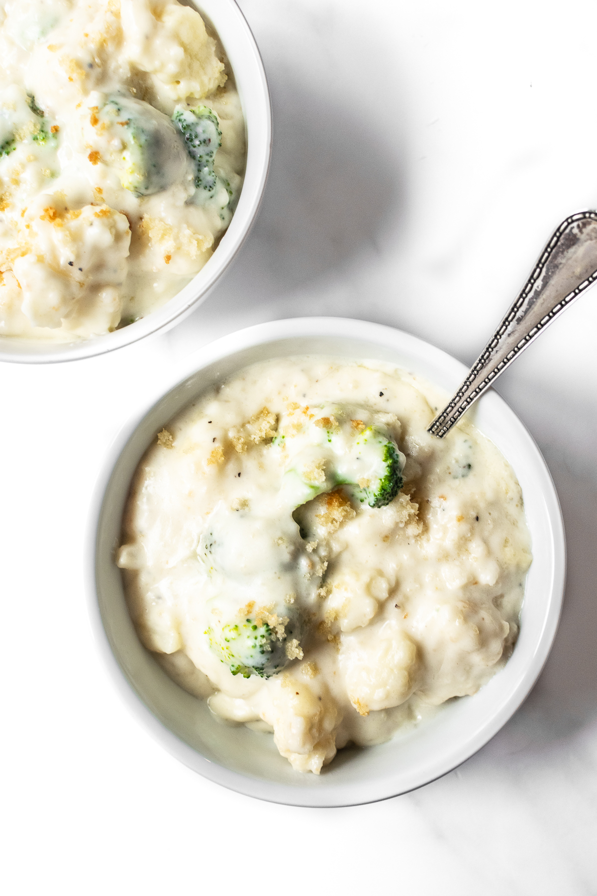 broccoli and cauliflower covered in a cheese sauce in a bowl with spoon