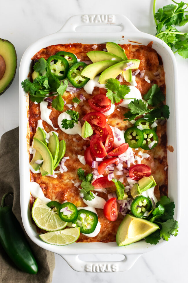 baked chicken enchiladas in a baking dish with toppings on a table