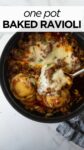 baked ravioli in a black pot with melted cheese and a serving spoon with a blue napkin.