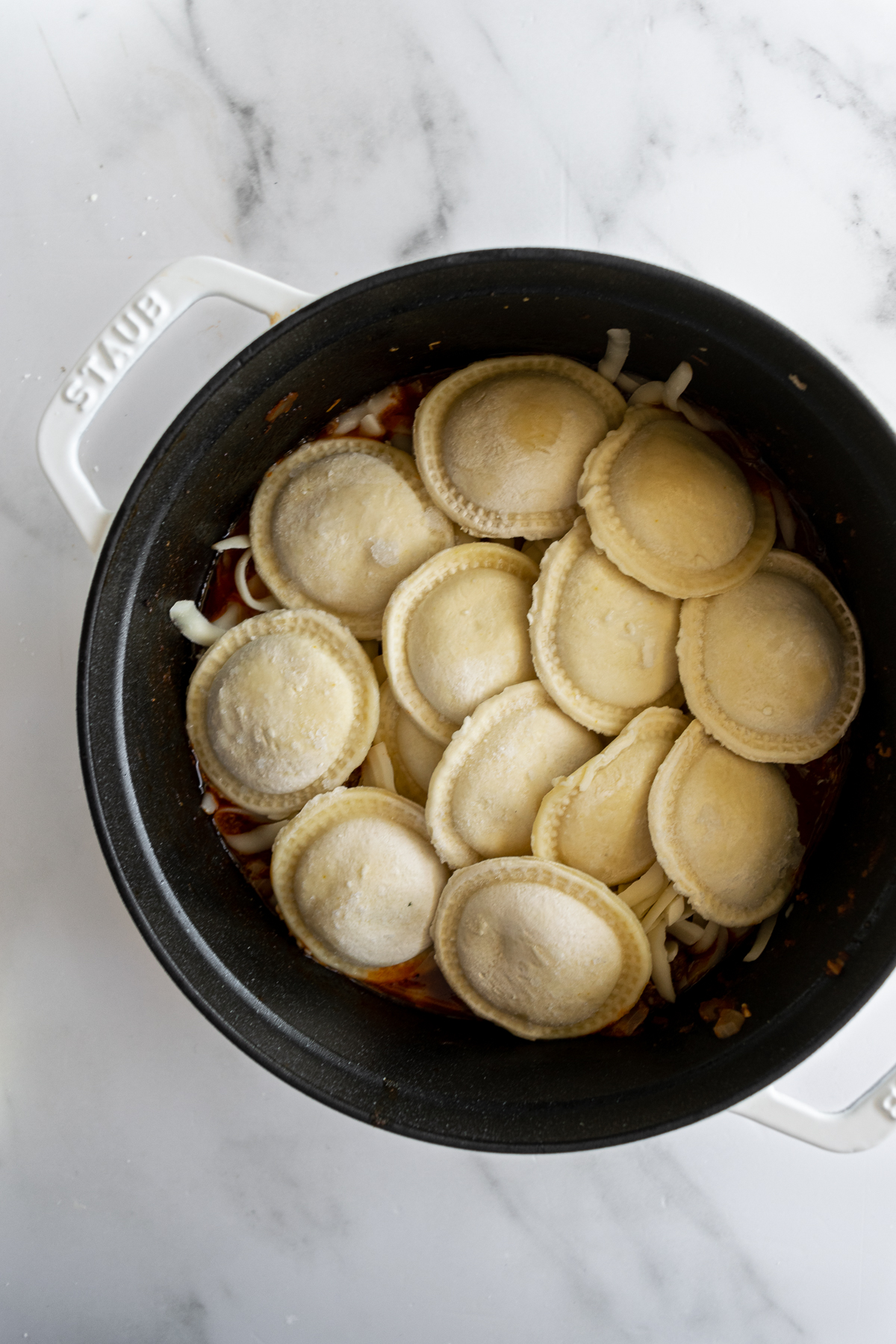 a single layer of uncooked ravioli in a black pot.