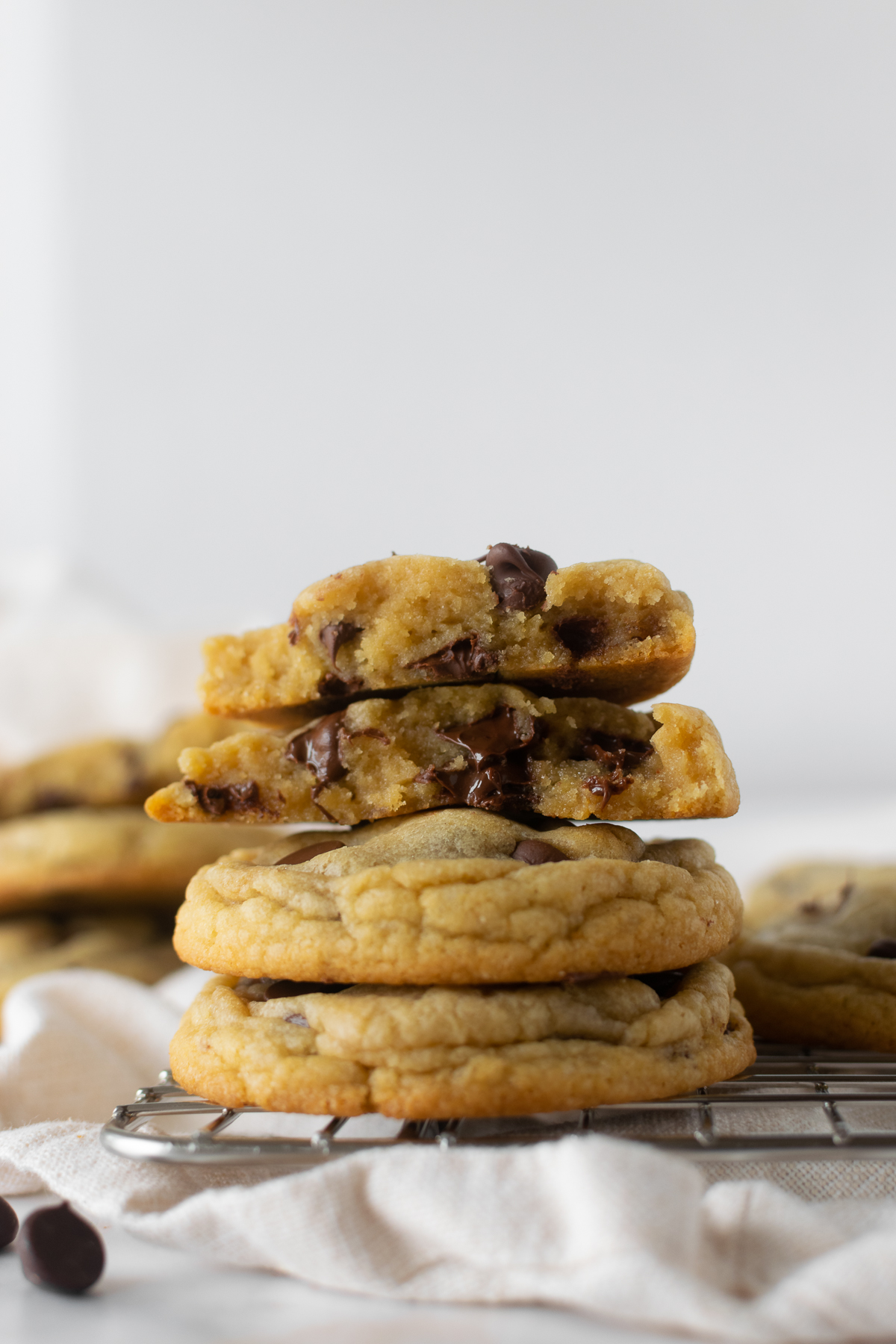 stacked chewy chocolate chip cookies on a cooling rack with a white napkin.