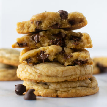stacked chewy chocolate chip cookies on a cooling rack with a white napkin.