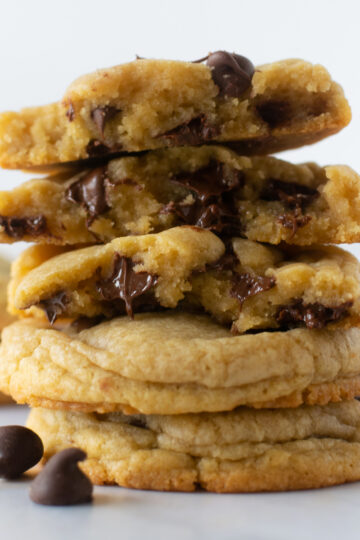 stacked chewy chocolate chip cookies on a cooling rack with a white napkin.
