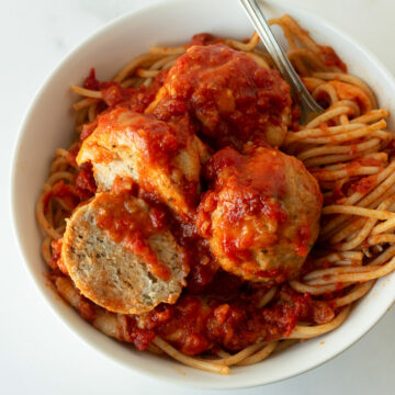 baked chicken parmesan meatballs in a white bowl with spaghetti and a fork.