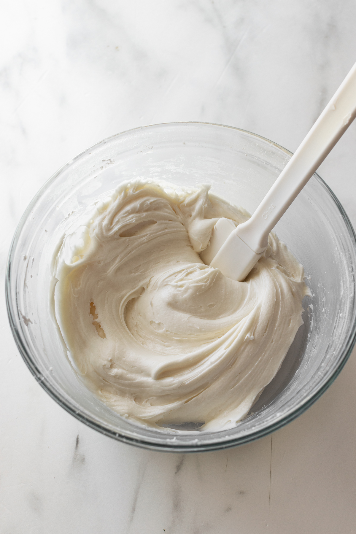 cream cheese frosting in a clear bowl with a white spatula.