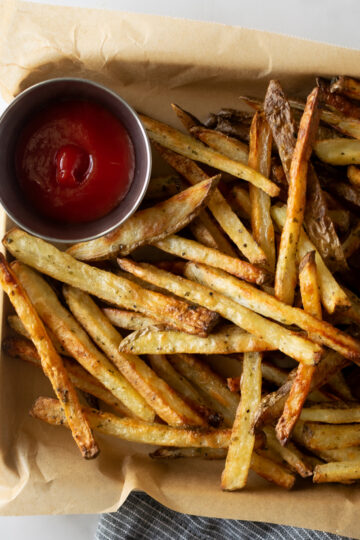 crispy baked french fries on a baking sheet with parchment paper with ketchup.