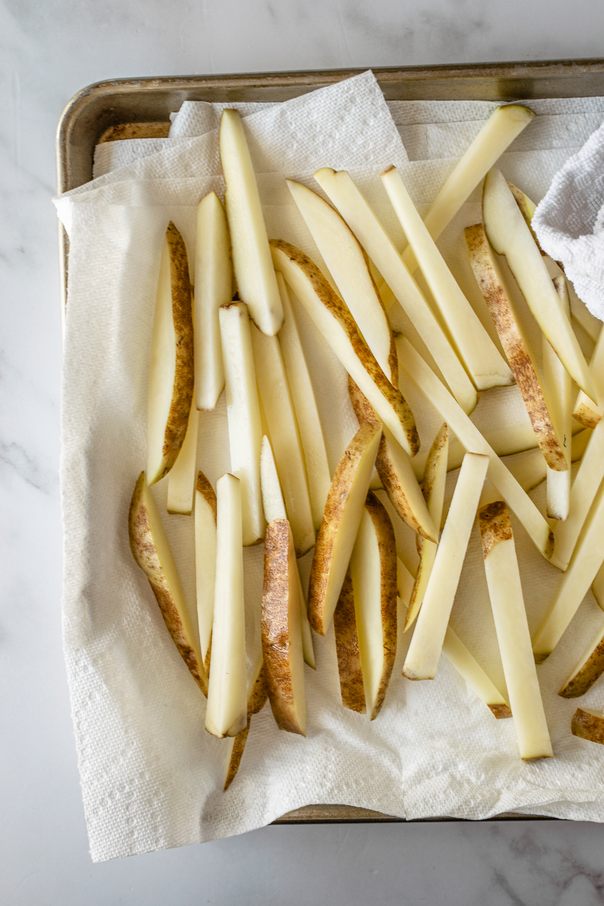 pre-baked sliced french fries sitting on paper towels on a baking sheet.