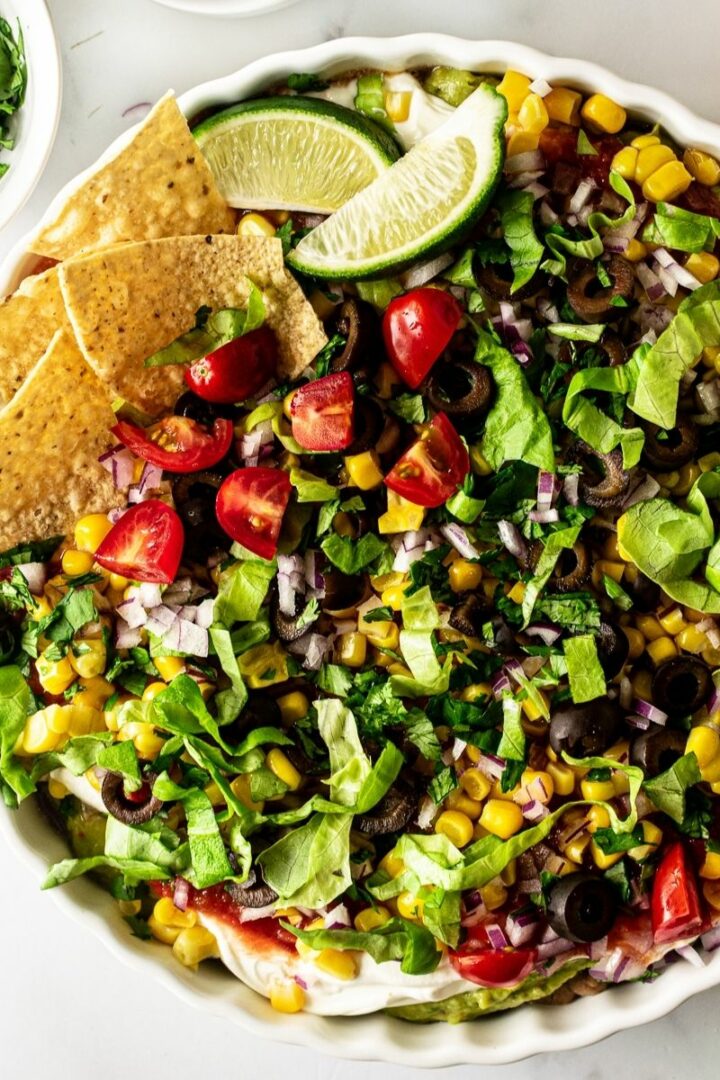 mexican 7 layer dip in a white bowl with chips.