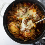 baked ravioli in a black pot with melted cheese and a serving spoon with a blue napkin.