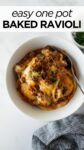 baked frozen ravioli in a white bowl with melted cheese and a fork.