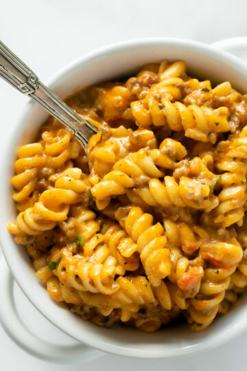 creamy beef pasta in a white bowl with a fork.