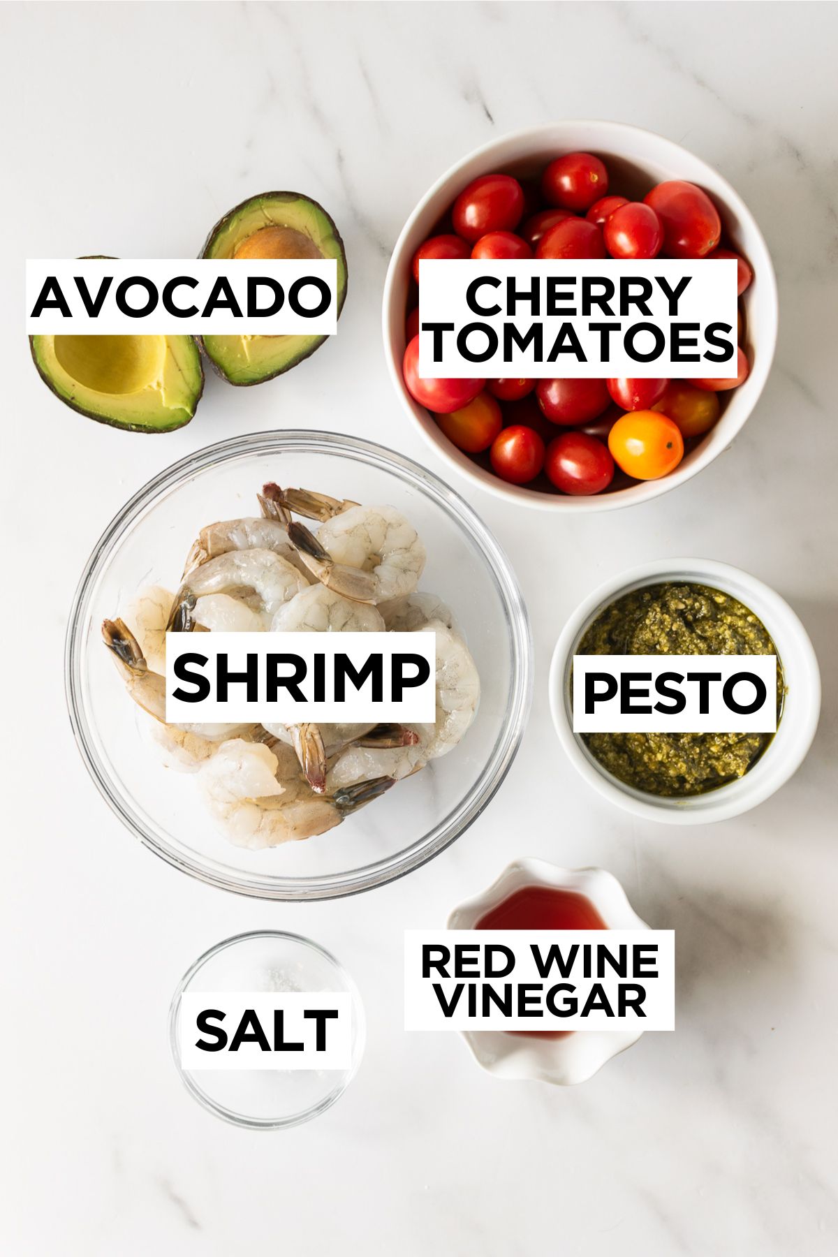 ingredients for pesto shrimp in bowls on a white table.
