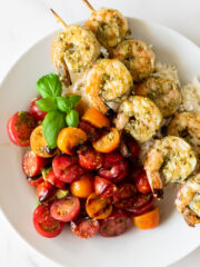 pesto shrimp on skewers with tomatoes in a white bowl.