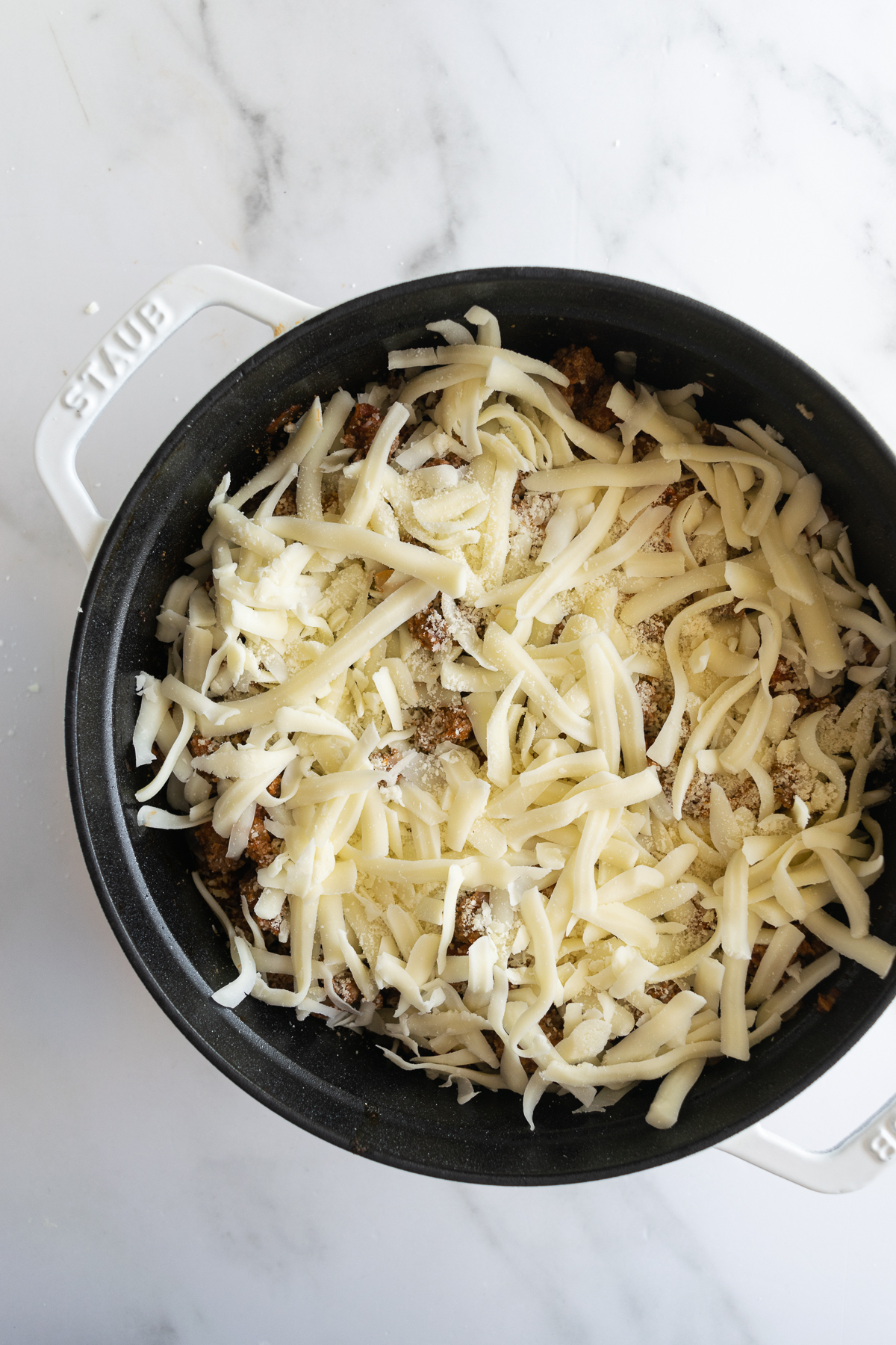 uncooked frozen ravioli in a black pot covered in shredded mozzarella cheese.