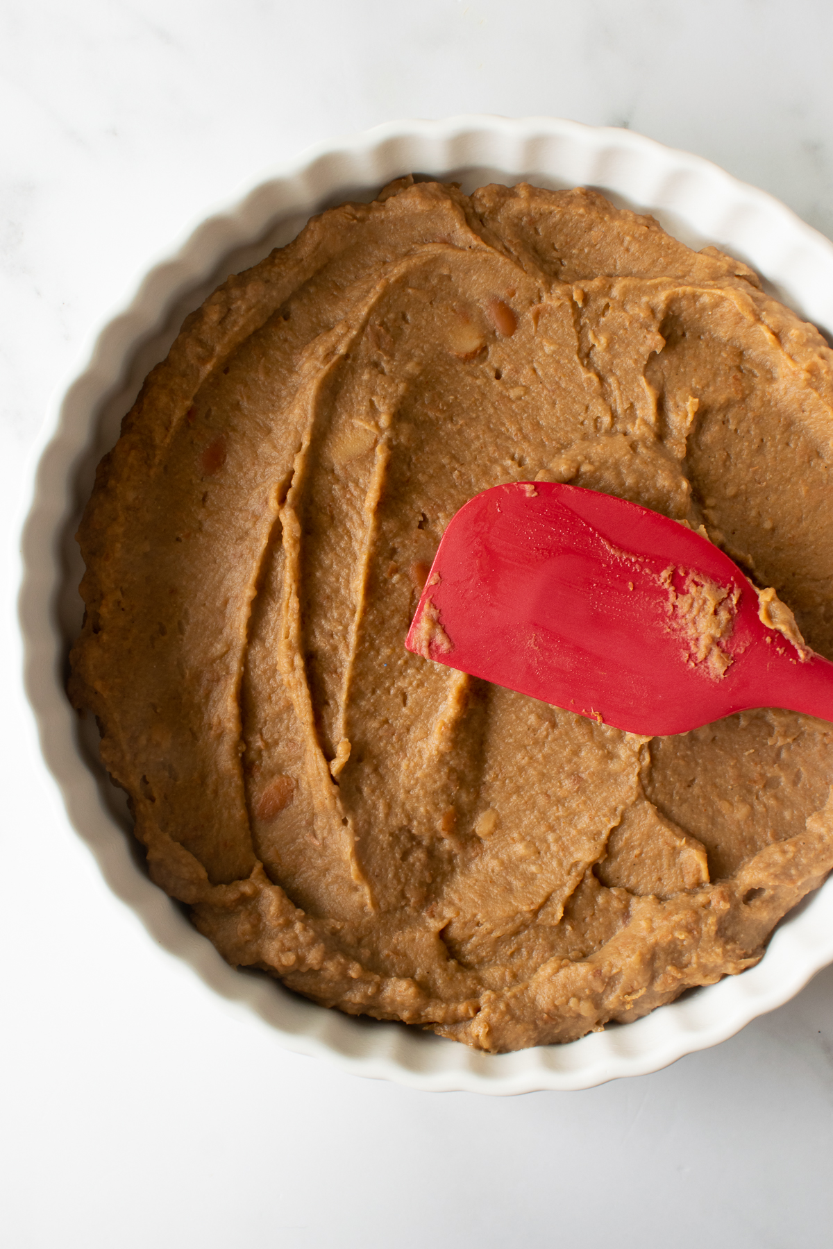 refried beans spread into a white pie dish with a red spatula.