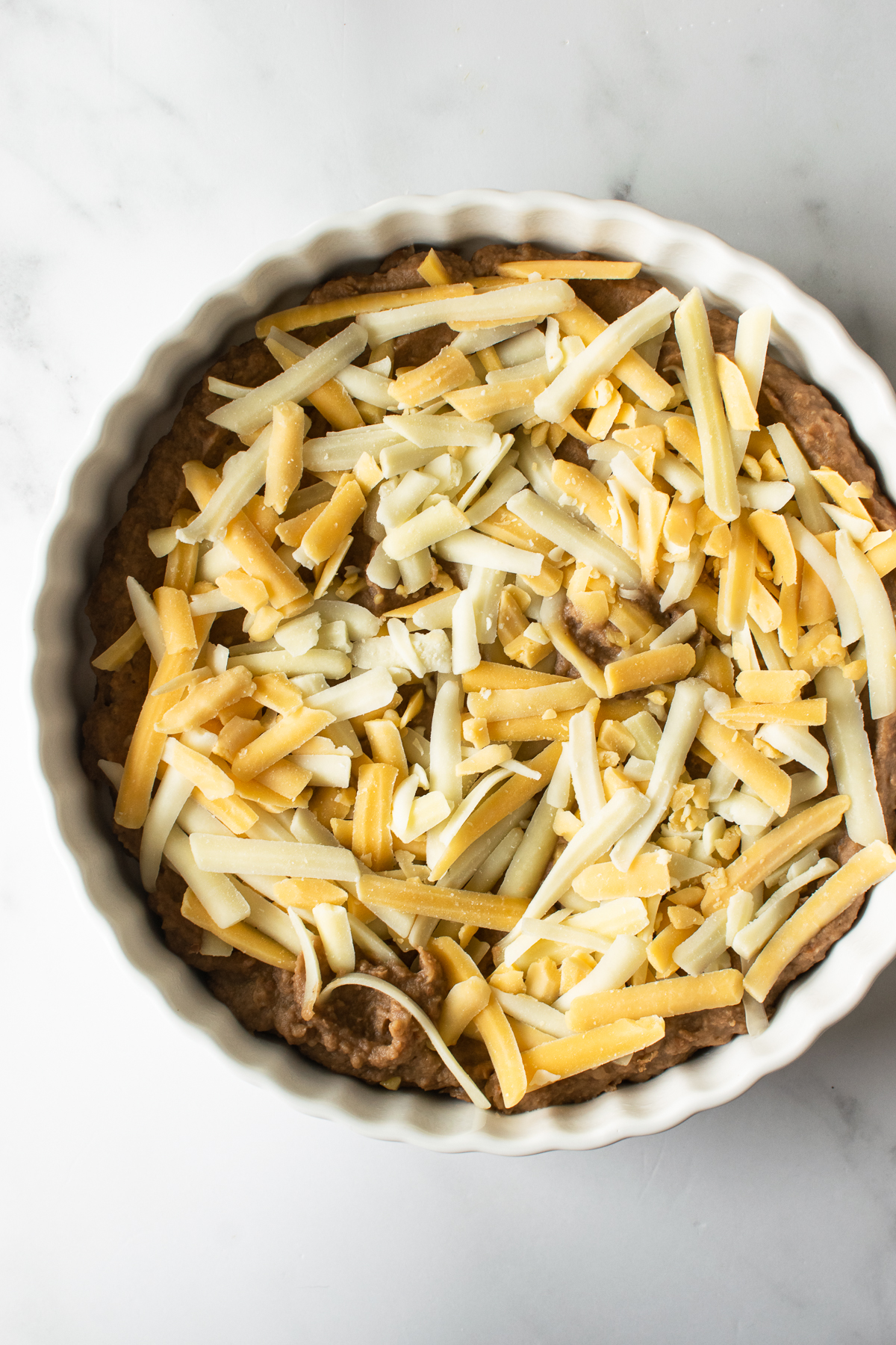 refried beans spread in a white pie dish with shredded cheese on top.