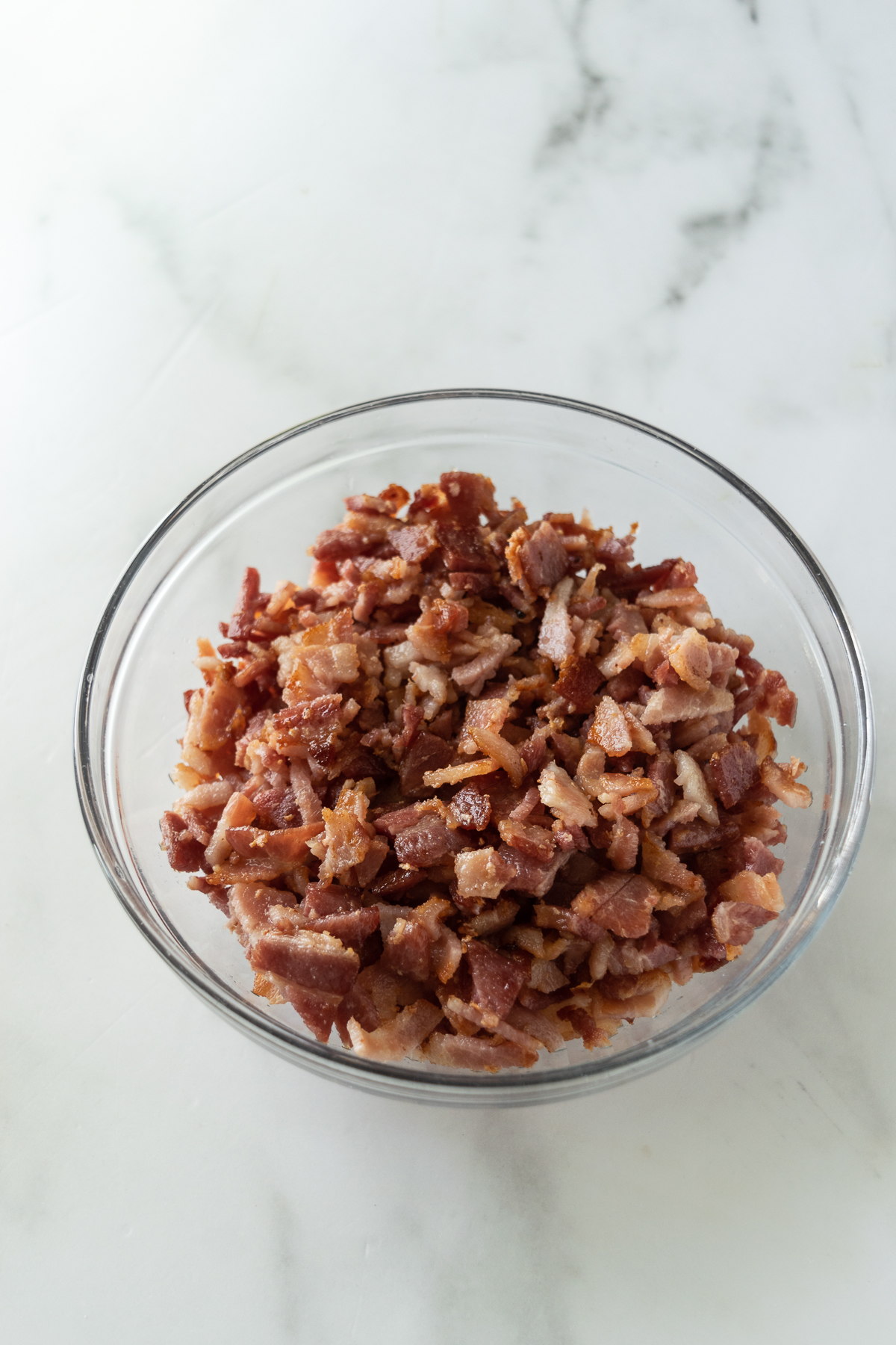 chopped bacon in a clear bowl on a white table.