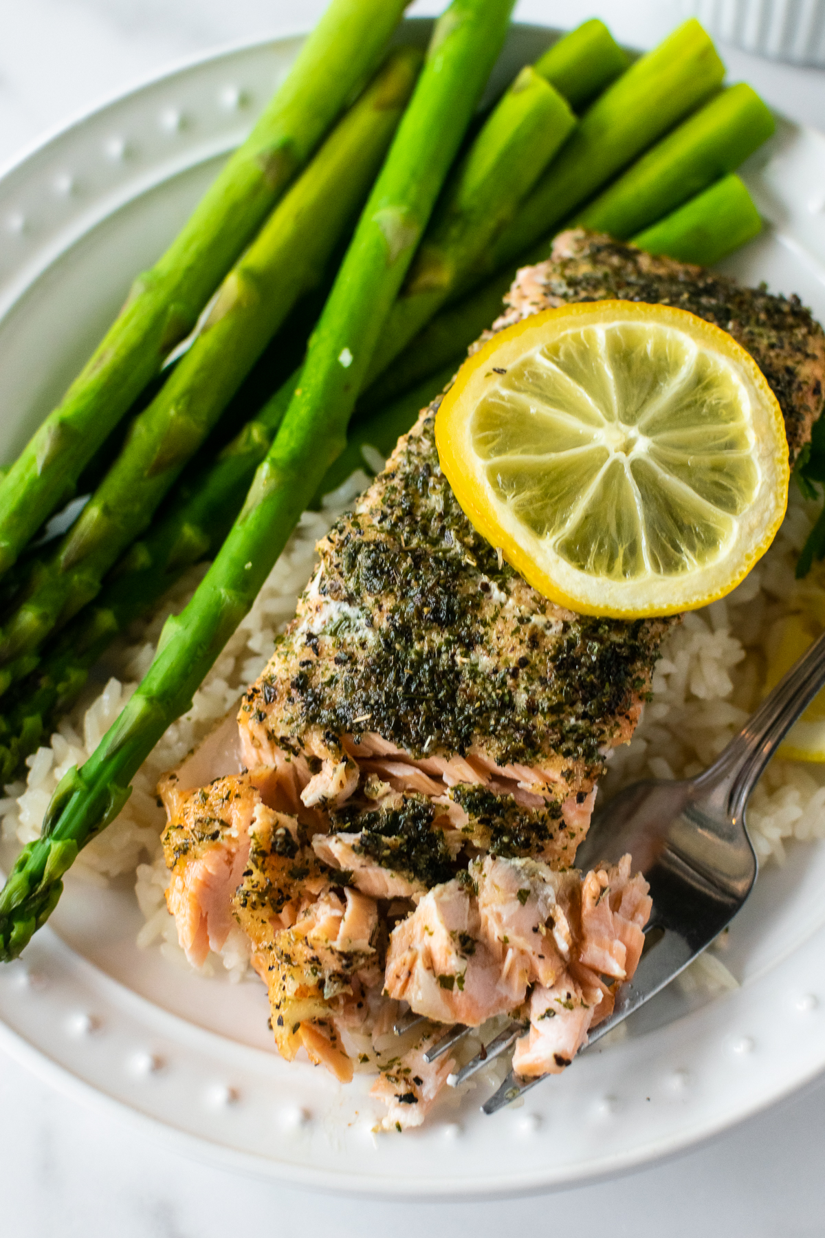 baked herb crusted salmon on a plate with a fork over rice and asparagus.