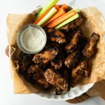 grilled chicken wings on a white plate with blue cheese on a cutting board.