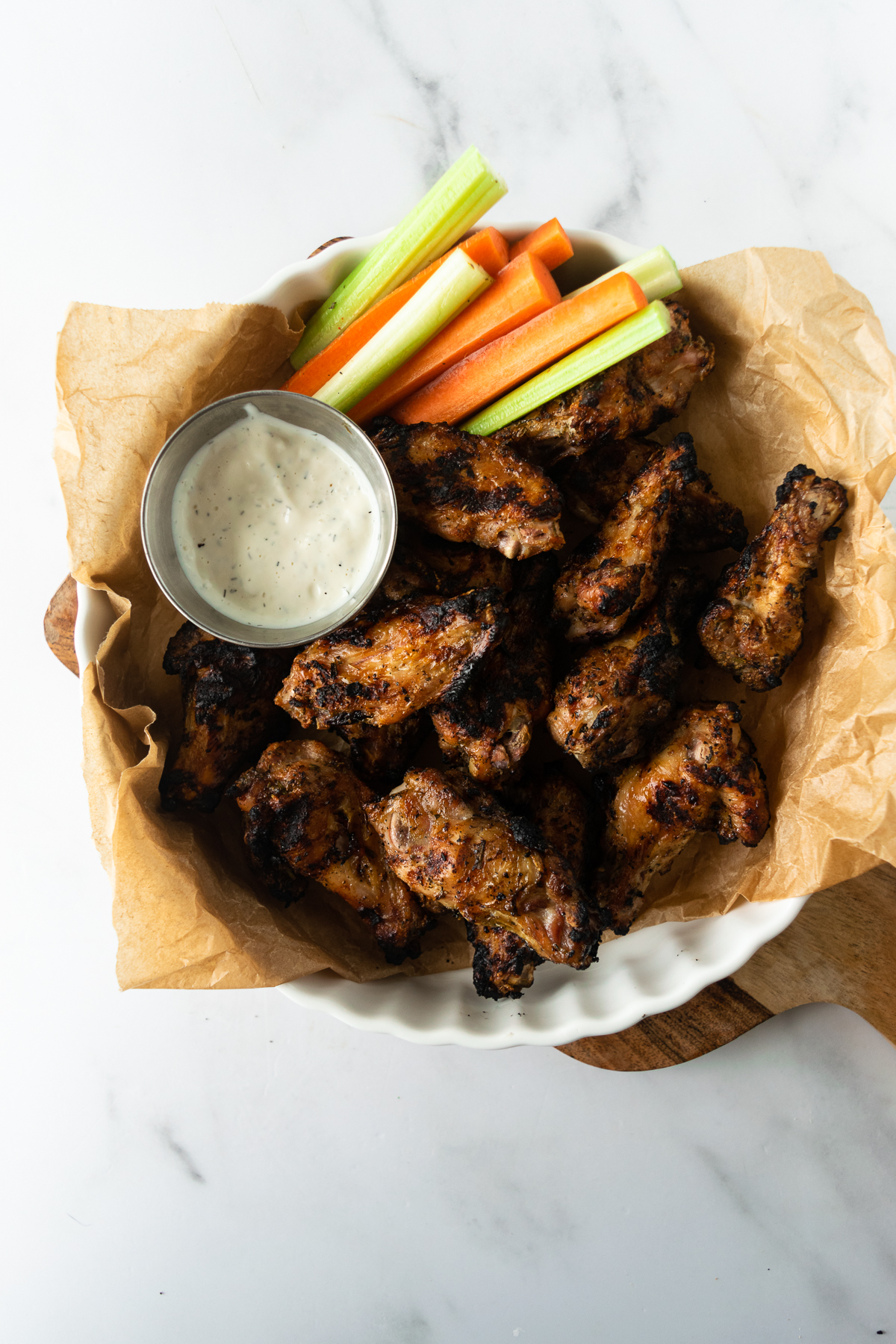grilled chicken wings on a white plate with blue cheese on a cutting board.