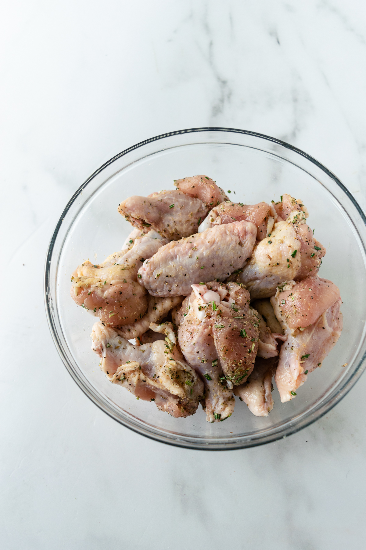 raw chicken wings in a bowl mixed with spice rub.