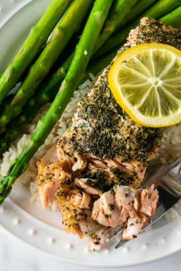 baked herb crusted salmon on a plate with a fork over rice and asparagus.