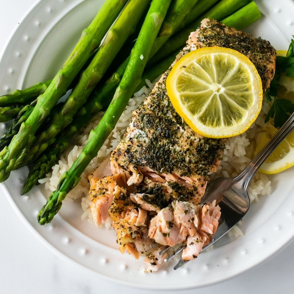 baked herb crusted salmon on a plate with a fork over rice and asparagus.