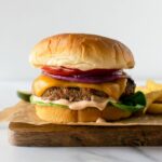 turkey burgers on a wood tray topped with melted cheese, lettuce, tomato and red onion.