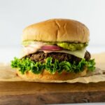 black bean burger on a wood board topped with lettuce, cheese, red onion, and guacamole.