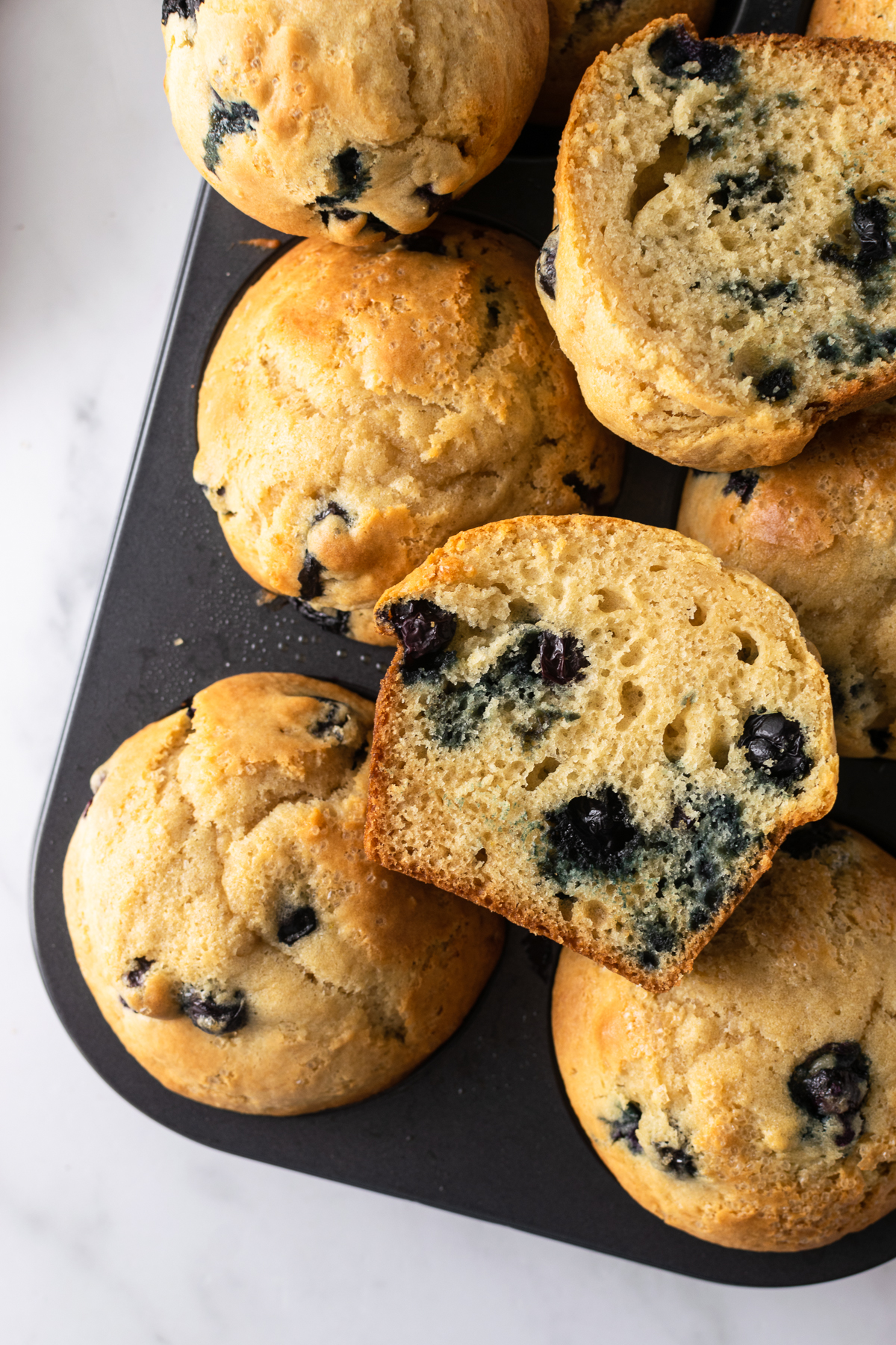 blueberry muffins in a muffin pan with a sliced muffin.