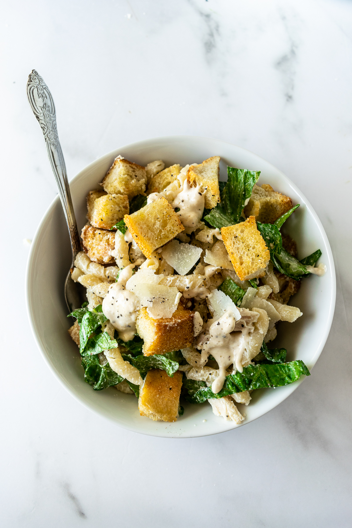chicken caesar pasta salad in a white bowl with a fork.