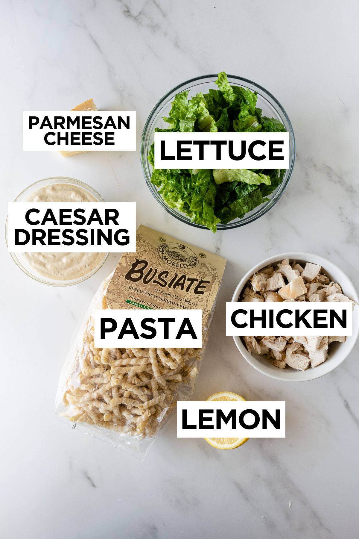 ingredients for chicken caesar pasta salad in bowls on a white table.
