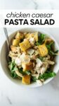 chicken caesar pasta salad in a white bowl with a fork with text overlay.