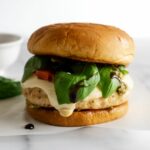 caprese burgers with melted mozzarella cheese, tomatoes and basil on a brioche bun.