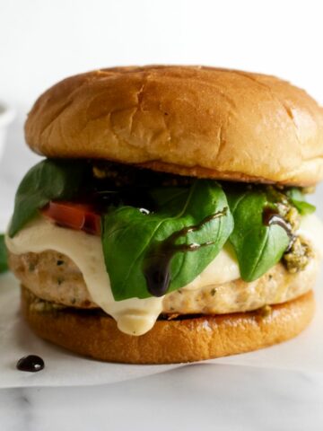 caprese burgers with melted mozzarella cheese, tomatoes and basil on a brioche bun.