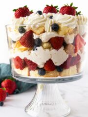 berry trifle in a glass trifle dish with pound cake, cheesecake filling, berries and whipped cream.