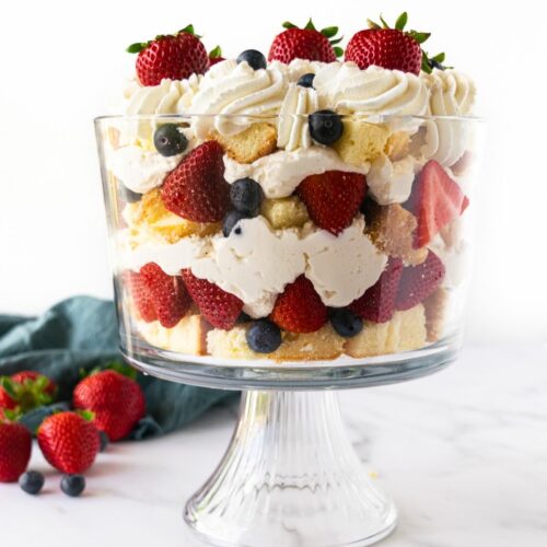 berry trifle in a glass trifle dish with pound cake, cheesecake filling, berries and whipped cream.