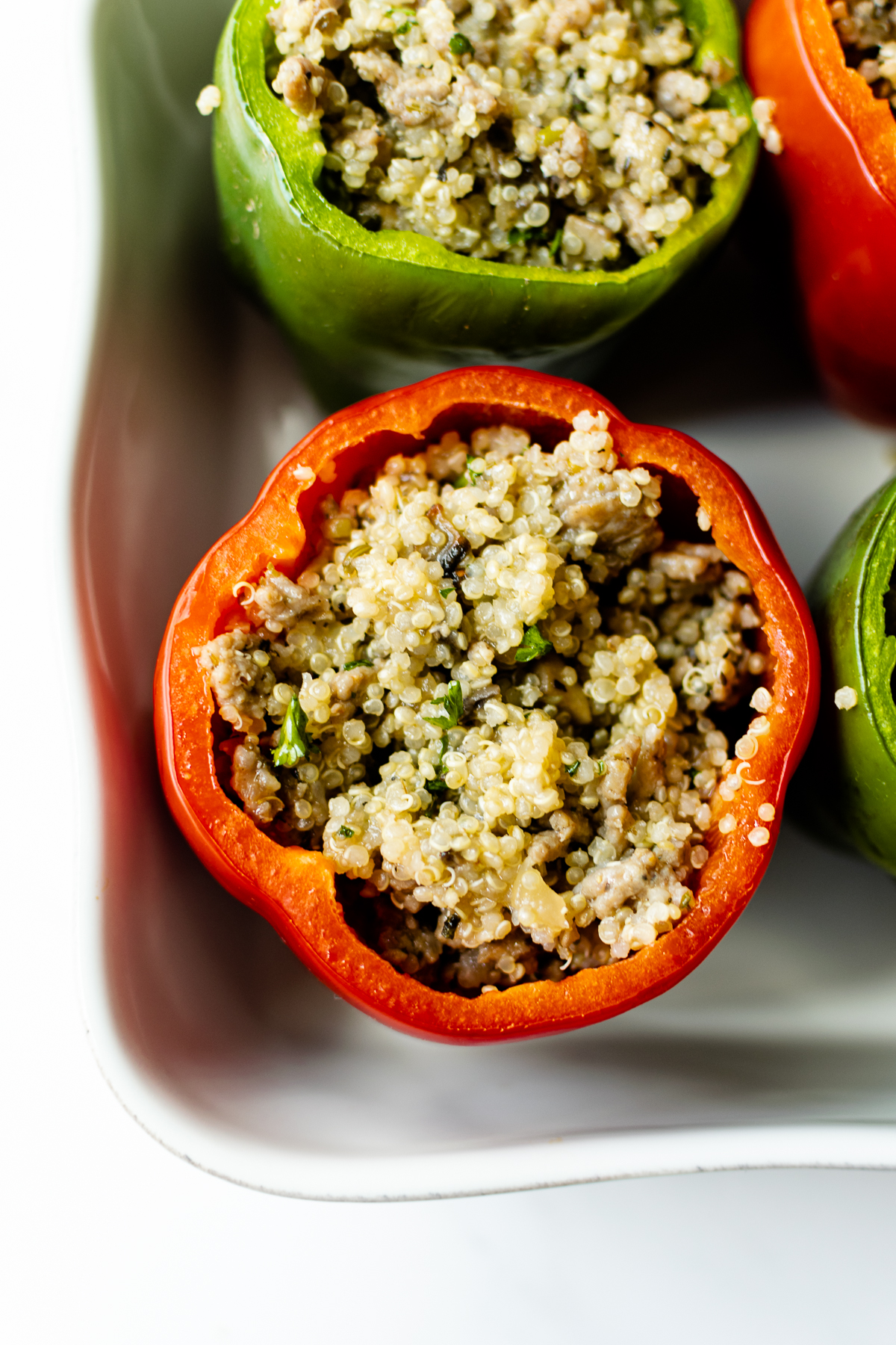 bell peppers stuffed with sausage and quinoa filling in a white baking dish.