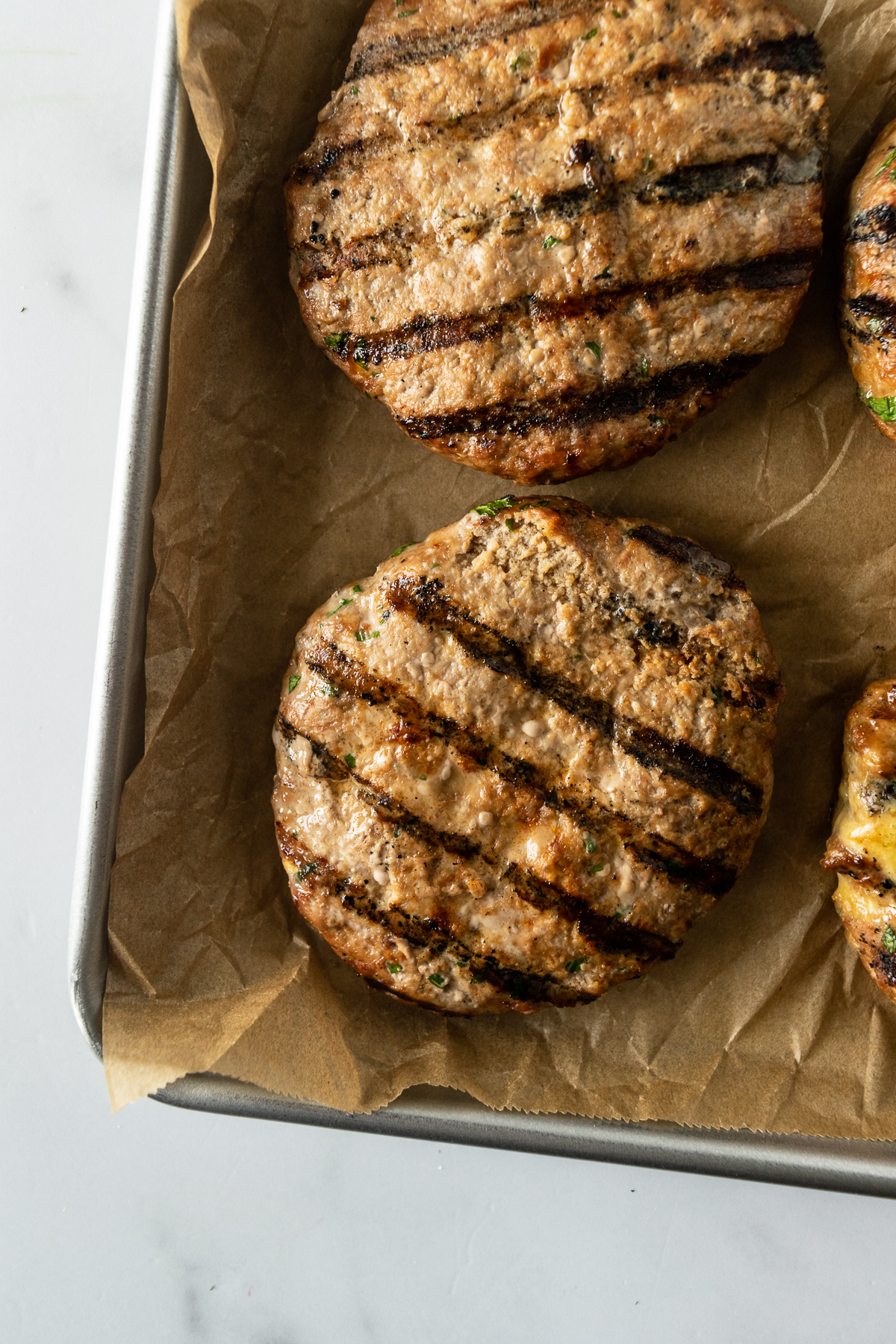 grilled turkey burgers on a baking sheet lined with brown parchment paper.