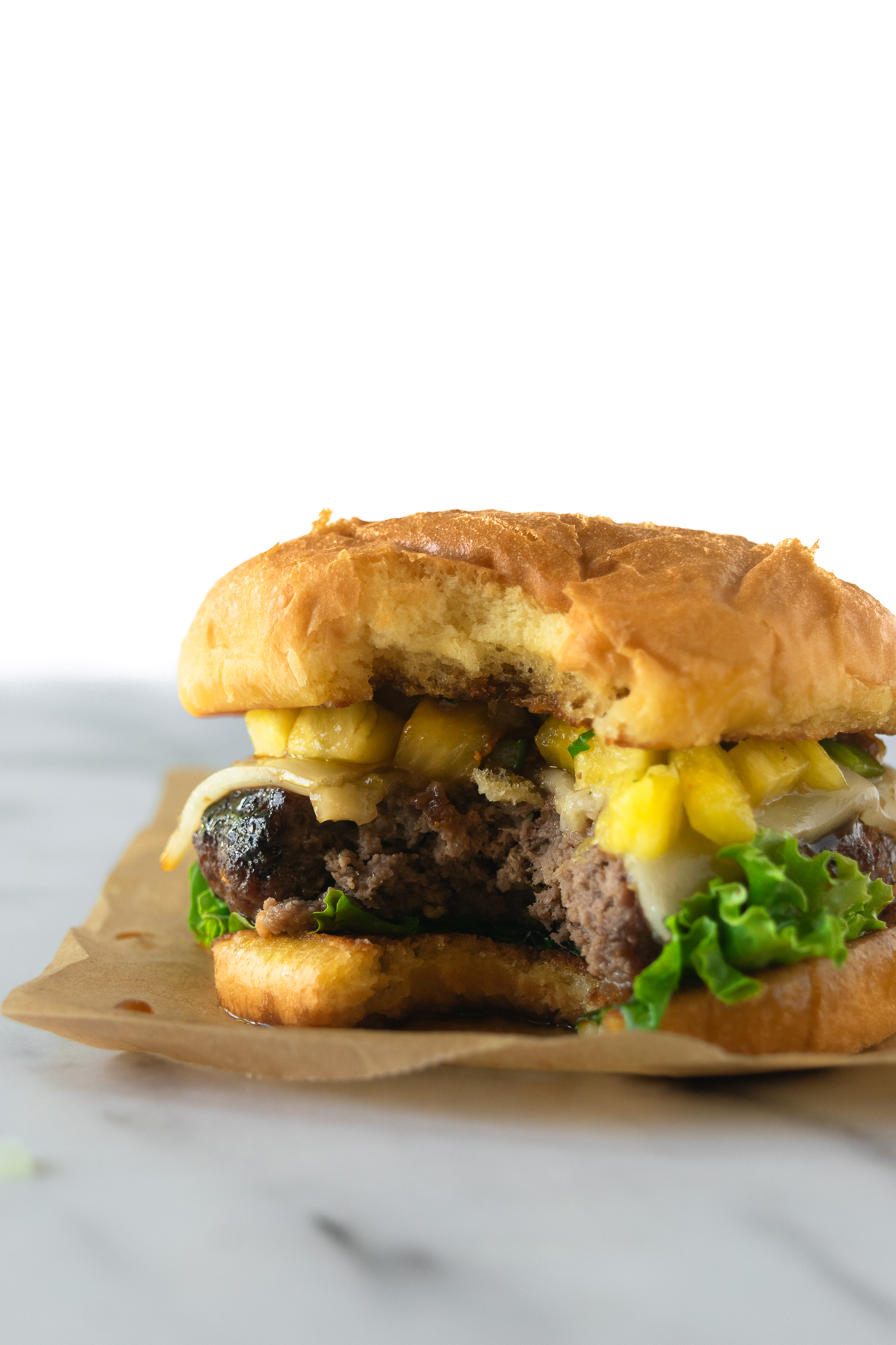 a bite from a teriyaki burger with melted cheese, lettuce, and pineapple salsa.