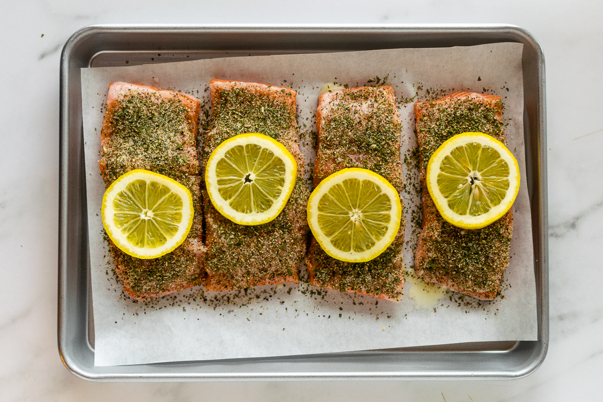 unbaked salmon filets on a baking sheet topped with sliced lemon.