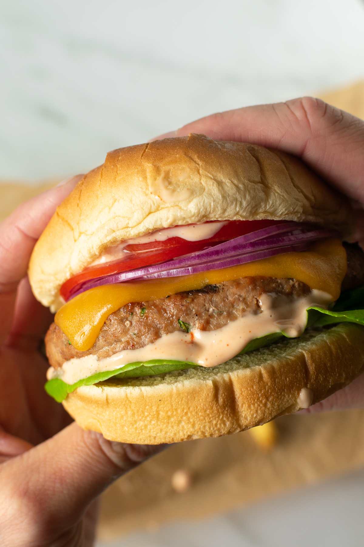 two hands holding a turkey burger topped with lettuce, tomato and red onion.
