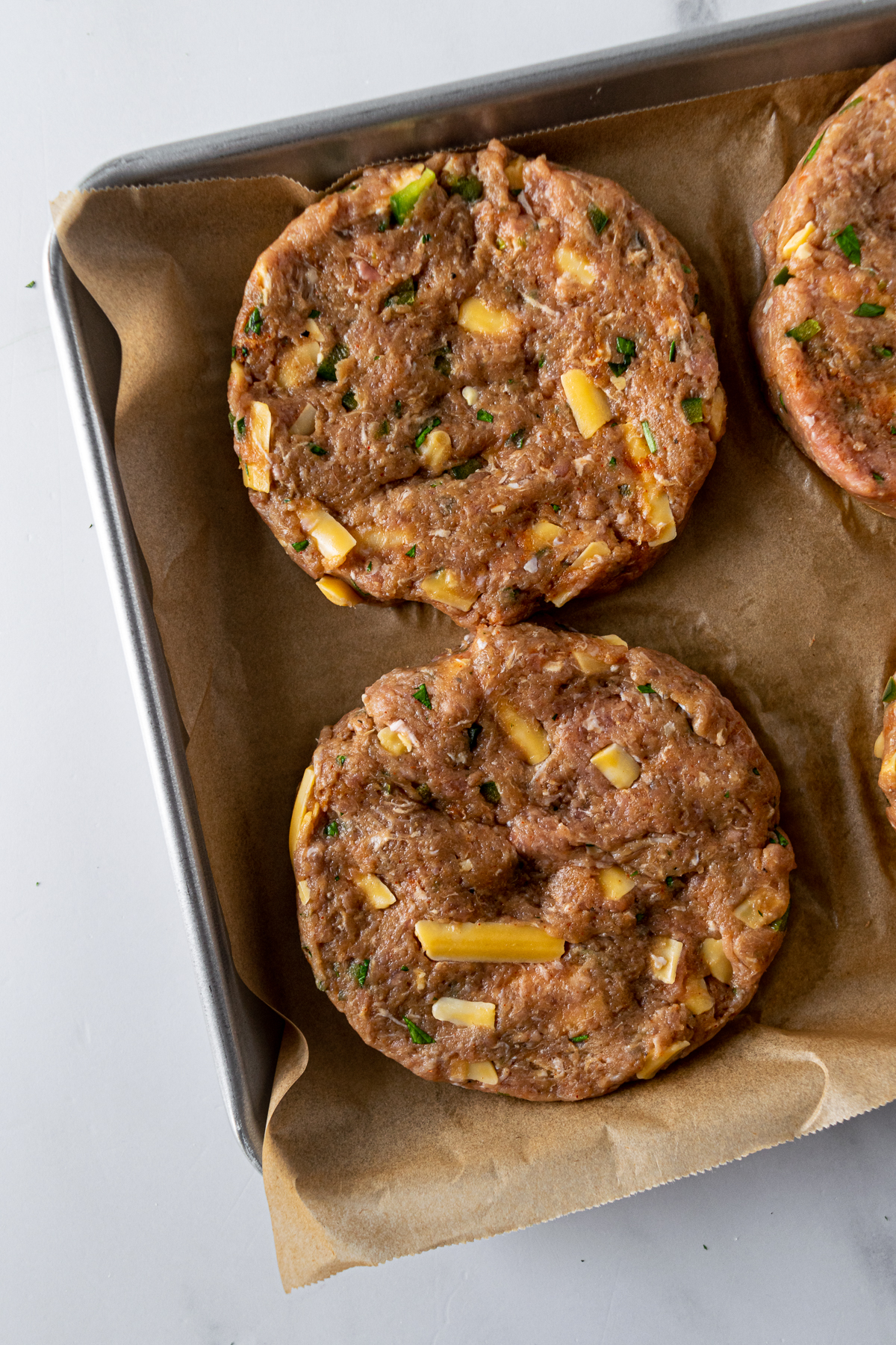 uncooked jalapeno turkey burger patties on a baking sheet lined with parchment paper.