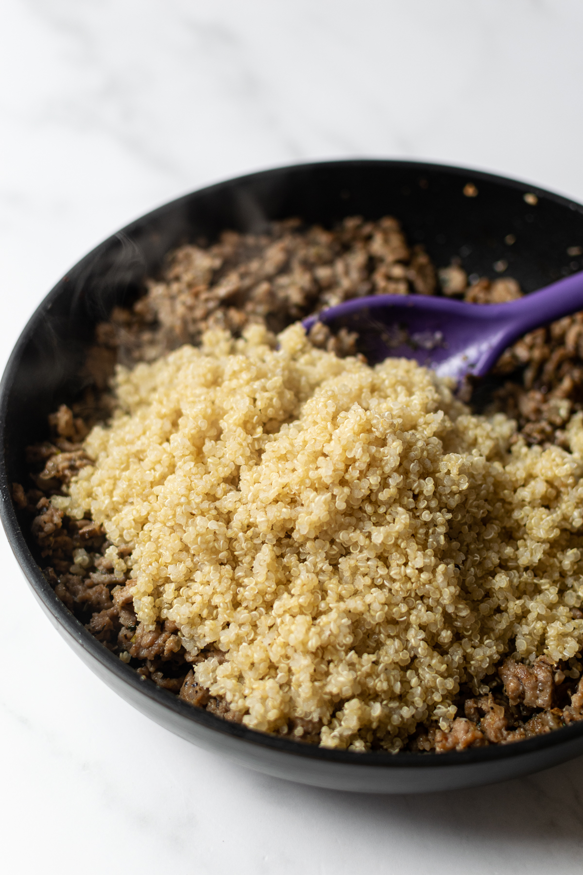 cooked ground sausage and quinoa in a black pan with a spoon.