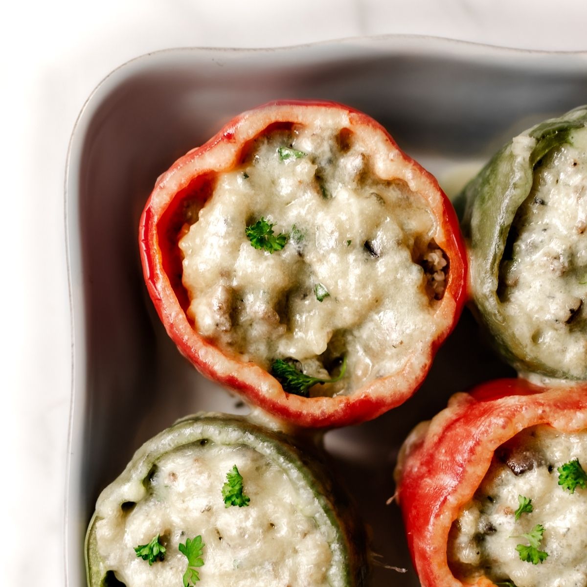 sausage stuffed peppers topped with melted cheese in a white baking dish.