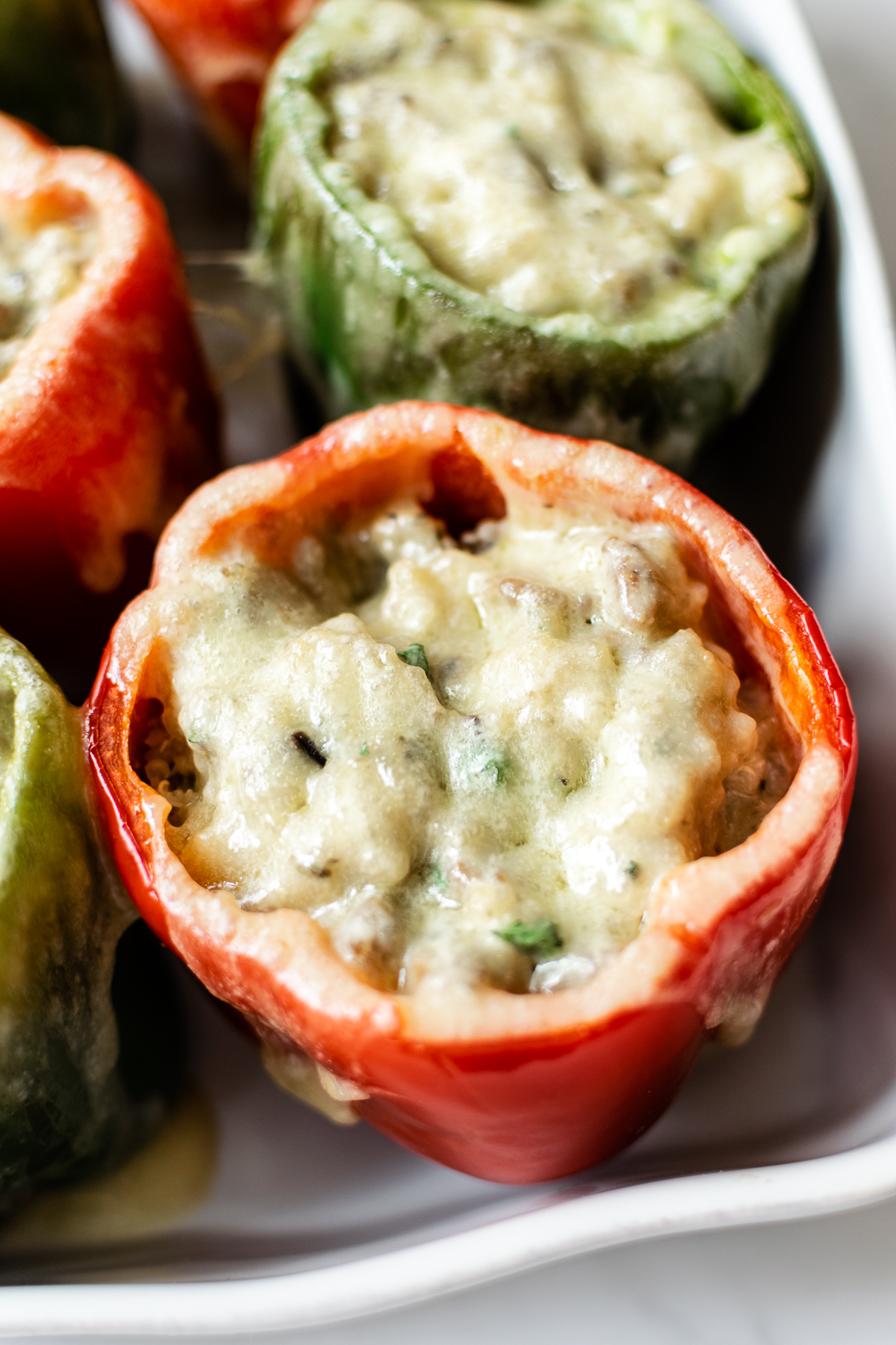 sausage stuffed peppers topped with melted cheese in a white baking dish.