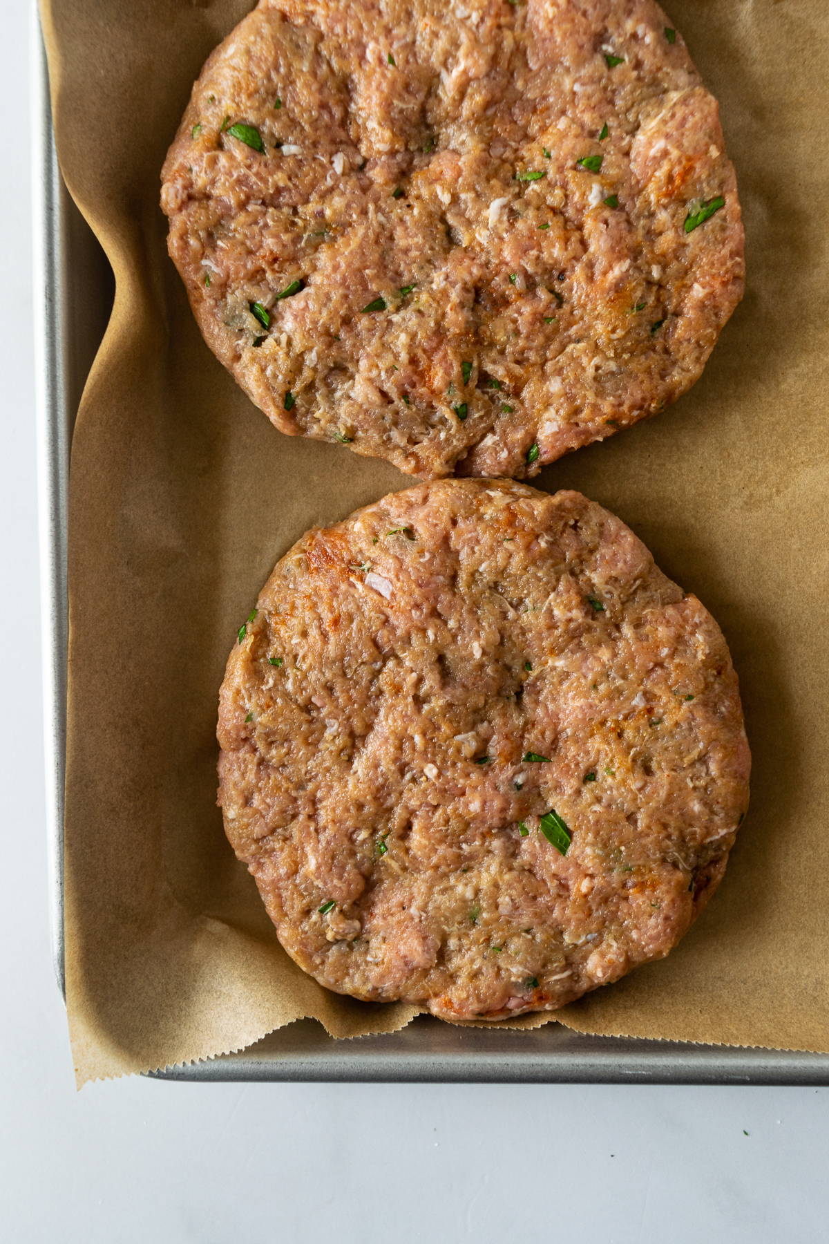 uncooked turkey burger patties on a baking sheet lined with parchment paper.