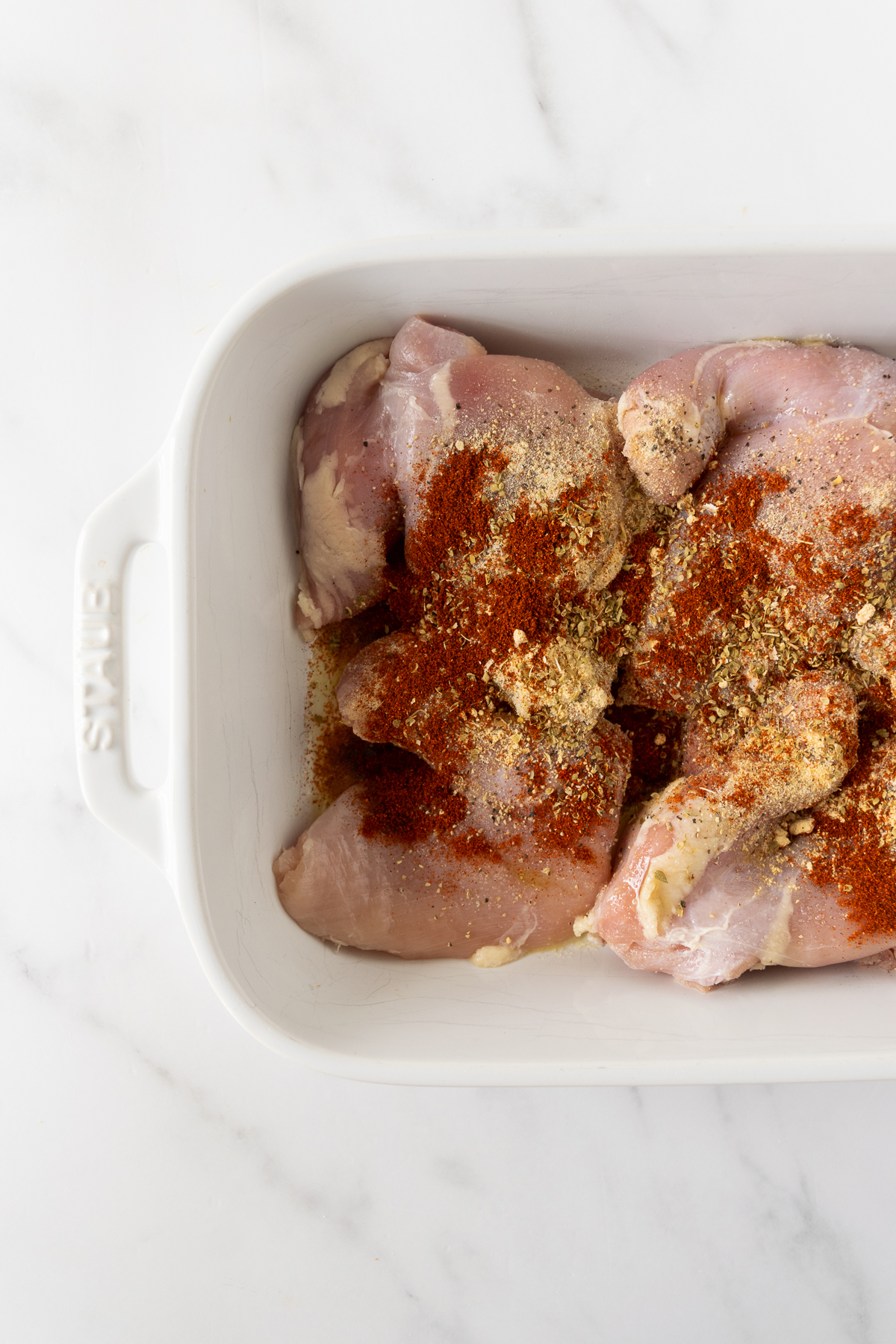 chicken thighs in a white baking dish with spices.